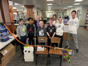 multiple students and teacher showcase their creative machine built using everday objects